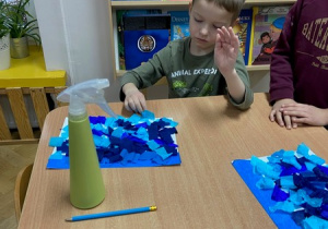Chłopiec układa niebieską bibułę pocięta w kwadraty na kartce papieru